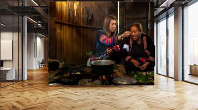 Asian family cooking and having dinner meal together at home. Hill tribe woman in traditional dress cooking food with herbal vegetable in traditional kitchen. Tribal culture and nature food concept. Wall mural