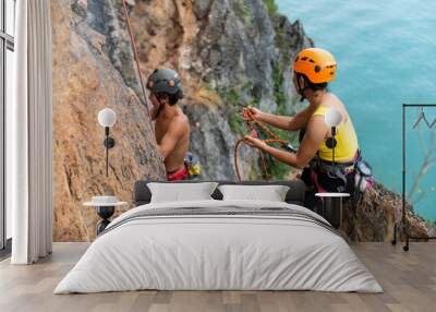 Asian man and woman climber climbing to rock mountain peak together at tropical island in sunny day. Strong male and female enjoy outdoor active lifestyle and extreme sport climbing on summer vacation Wall mural