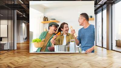 Asian people friends enjoy cooking pasta in cooking pan with talking together in the kitchen at home. Man and woman having dinner party meeting celebration eating food together on holiday vacation Wall mural