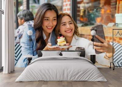 Asian woman friends using smartphone selfie together while sitting at outdoor coffee shop eating bakery and drinking coffee in urban city street. Beautiful female enjoy outdoor lifestyle in the city Wall mural