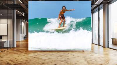 Asian woman surfer surfing and riding surfboard the wave in the sea at tropical beach in sunny day. Healthy female enjoy outdoor activity lifestyle and water sport exercise surfing on summer vacation Wall mural