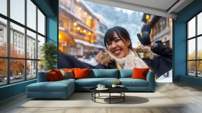 Asian woman tourist using mobile phone taking selfie during travel onsen area Ginzan Onsen in Yamagata prefecture, Japan in snow day. Attractive girl travel local village landmark on winter vacation Wall mural