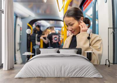 Asian woman using mobile phone and listening to the music on earphones during travel on tram in the city. Attractive girl enjoy urban lifestyle in the city with using wireless technology on device. Wall mural