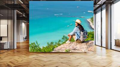 Asian woman with backpack travel at tropical island and resting on mountain peak in summer sunny day. Attractive girl enjoy outdoor lifestyle looking beautiful ocean nature on beach holiday vacation. Wall mural