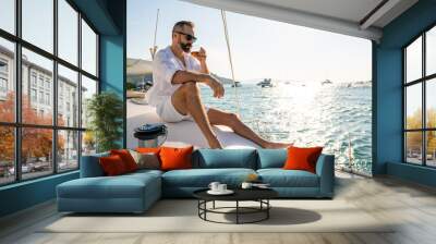 Caucasian man enjoy outdoor luxury lifestyle with alcoholic drinks while catamaran boat sailing at summer sunset. Handsome male relaxing outdoor leisure activity with tropical travel vacation trip Wall mural