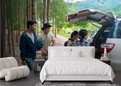 Group of Asian people friends enjoy outdoor lifestyle road trip and camping together on summer holiday travel vacation. Man and woman taking off camping supplies from car trunk at natural park. Wall mural