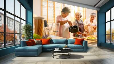 Group of Happy Asian senior women having dinner together at home. Elderly woman friends enjoy healthy lifestyle cooking and making vegan food vegetables salad with using air fryer in the kitchen. Wall mural