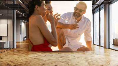 Group of man and woman friends enjoy party drinking champagne with talking together while catamaran boat sailing at summer sunset. Male and female relax outdoor lifestyle on tropical travel vacation Wall mural