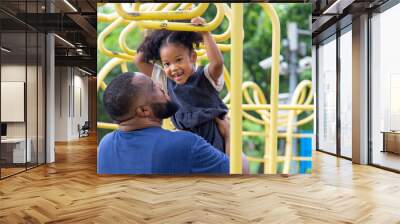 Happy affectionate mixed race family. African man father carrying little daughter playing at playground in the park. Dad and cute child girl enjoy and having fun together in outdoor weekend vacation. Wall mural