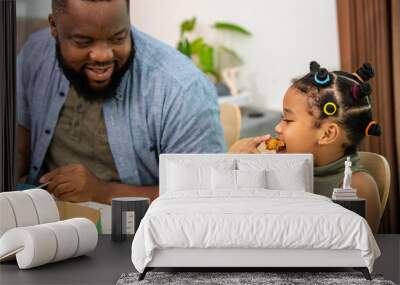 Happy African family parents and two little daughter eating fried chicken and pizza for dinner together. Father and mother and cute child girl kid enjoy eating and sharing a meal together at home Wall mural