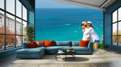 Happy Asian family couple enjoy outdoor lifestyle travel tropical island on summer holiday vacation. Husband and wife embracing each other at mountain peak and looking to blue ocean in sunny day. Wall mural