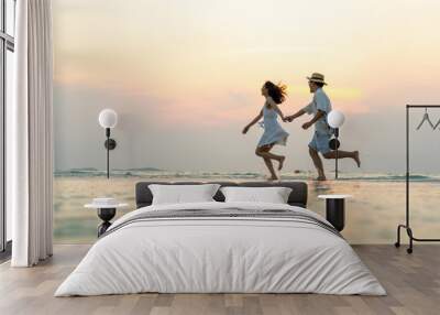 Happy Asian family couple walking and playing in sea water together on tropical beach at summer sunset on beach vacation. Husband and wife relax and enjoy outdoor lifestyle on holiday travel vacation Wall mural