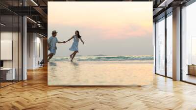 Happy Asian family couple walking and playing in sea water together on tropical beach at summer sunset on beach vacation. Husband and wife relax and enjoy outdoor lifestyle on holiday travel vacation Wall mural