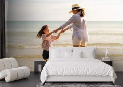 Happy Asian family on beach vacation. Mother and little daughter walking and playing together on tropical beach at summer sunset. Mom and child girl kid enjoy and fun outdoor lifestyle on the beach Wall mural