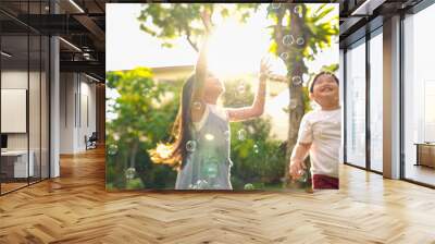 Happy Asian family relationship at home. Mother with little daughter and son playing soap bubbles in backyard garden. Joyful parent with two child kids relax and having fun weekend activities together Wall mural