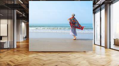 Happy Asian senior woman in blue dress walking on tropical island beach at summer sunset. Elderly retired woman relax and enjoy outdoor lifestyle activity in summer beach holiday travel vacation. Wall mural