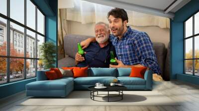 Happy Caucasian family senior father and adult son watching sport game on TV with drinking beer together in home living room. Excited dad and son sport fans cheering sports team for winning the match. Wall mural