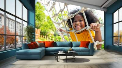 Happy Little African child girl playing and climbing rope net at outdoor playground in the park on summer vacation. Kindergarten children kid enjoy and fun outdoor activity and exercising at park. Wall mural