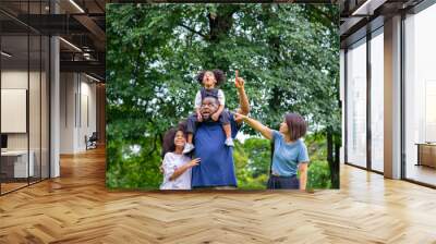 Happy mixed race family African father and Asian mother with two little daughter holding hands walking together in park. Mom and dad with child girl kid enjoy and having fun outdoor lifestyle activity Wall mural