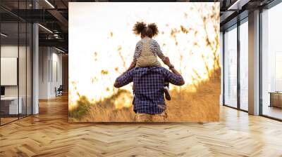 Happy mixed race family on holiday vacation. Smiling father and little daughter carrying and hiking together on meadow hill in summer. Parent with cute child girl relax and enjoy outdoors lifestyle. Wall mural