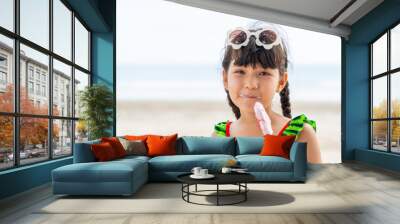 Little Asian child girl in swimwear eating ice cream while playing with family on tropical beach in sunny day. Happy little girl enjoy and fun outdoor activity lifestyle on summer holiday vacation Wall mural