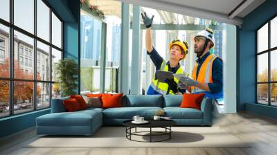 Professional Asian man and woman teamwork engineer in safety uniform working at outdoor construction site rooftop. Industrial technician worker maintenance checking building exterior plumbing systems. Wall mural