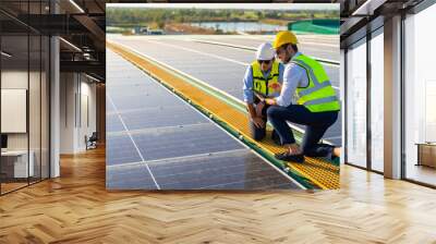 Professional man engineer using digital tablet maintaining solar cell panels together on building rooftop. Technician team working on ecological solar farm. Renewable clean energy industry concept. Wall mural