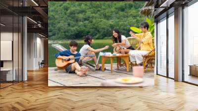 Young Asian man and woman enjoy outdoor lifestyle travel nature forest mountain on summer holiday vacation. Happy generation z people friends playing guitar and doing hobbies at lake house balcony. Wall mural