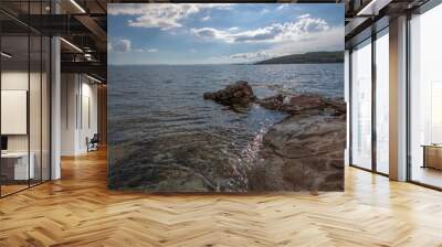 Image of island from rocky shore. Blue cloudy sky. Wall mural