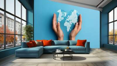 Female hands holding a map of the world isolated on blue background. Flat lay, top view, love shape, earth day concept Wall mural