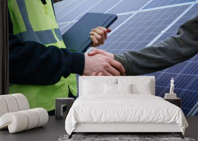 Close-up view of two individuals shaking hands in front of solar panels. Wall mural