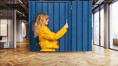 middle-aged blonde woman with yellow outfit on blue background and mobile phone Wall mural