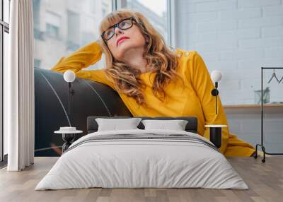 serious adult woman looking out the window sitting on the sofa at home Wall mural