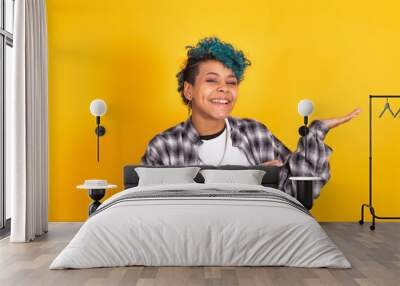 young african american woman with blue curly hair pointing at yellow background Wall mural