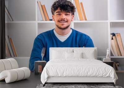 young man at table smiling with cutlery and knife Wall mural