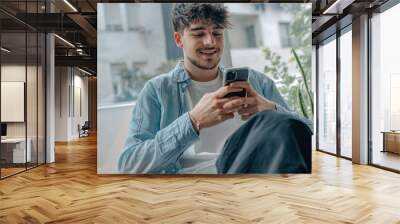 young man with mobile phone sitting on the sofa at home Wall mural