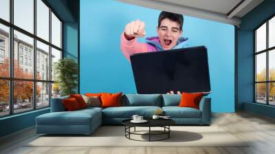 young teenage man or student with laptop isolated on background with surprise or success expression Wall mural