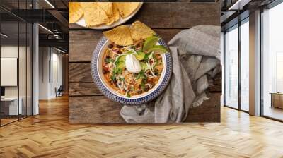 Chicken tortilla soup with sour cream, avocado, lime, tortilla chips and napkin on wooden table, from above Wall mural