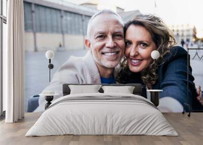 Affectionate mid adult happy couple having fun taking a selfie portrait together on the street. Middle aged man and woman friends smiling looking at camera. Wall mural