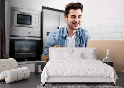 Handsome young man working with a laptop and smiling at the kitchen with a cup of tea - Cheerful, success and business concept Wall mural