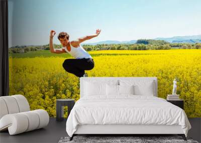 Portrait of young homosexual boy jumps in a yellow rapeseed field. Concept of a good mood and summer vacation. Wall mural