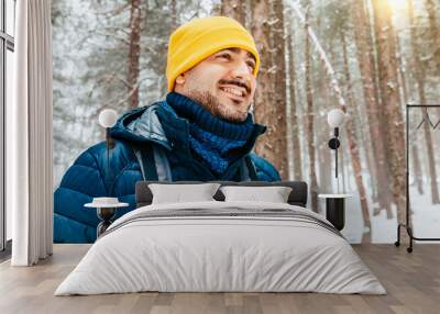 Winter hike on snow mountain young happy hiker man walking. Europe travel adventure trek in nature landscape. Young bearded person wearing yellow hat, blue jacket for cold weather and bag. Wall mural