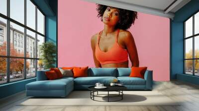 attractive young black african american adult woman in sports outfit looking at camera and posing isolated on pink background Wall mural