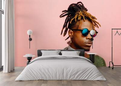 Close up portrait of a young man in green with dreadlocks and blue sunglasses, isolated on pink Wall mural