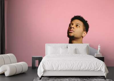 Close up portrait of a young man looking up and left with interest, , isolated on pink studio background Wall mural