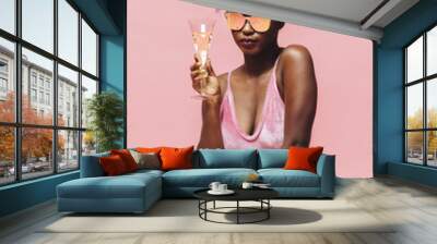 Cool girl with sunglasses holding champagne glass, isolated on pink Wall mural