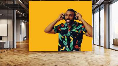 handsome mid adult bearded african american man with headphones listening music posing on yellow background looking away at copy space studio shot Wall mural