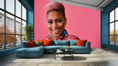 Portrait of a happy stylish young woman with pink hair and colorful fashion jacket on pink background Wall mural