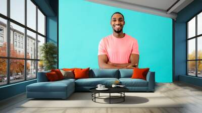 Portrait of a happy young man smiling with arms crossed, against blue studio background Wall mural