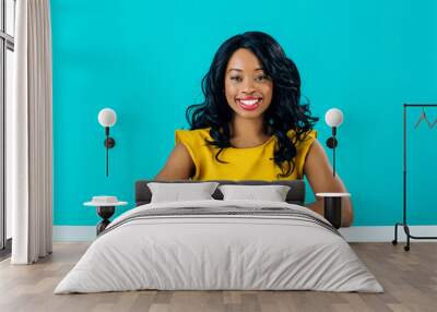 Portrait of a happy young smiling woman sitting behind desk  with arms crossed isolated on blue Wall mural